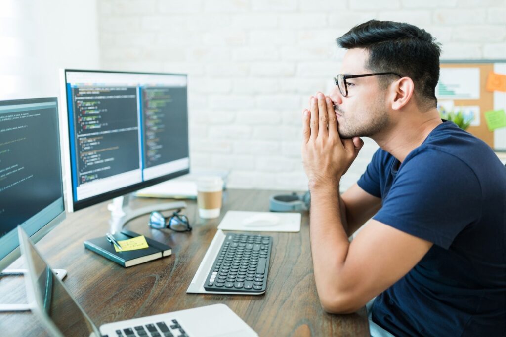 Programmer setting up ERP computer software thinking in front of his computer screens and laptop